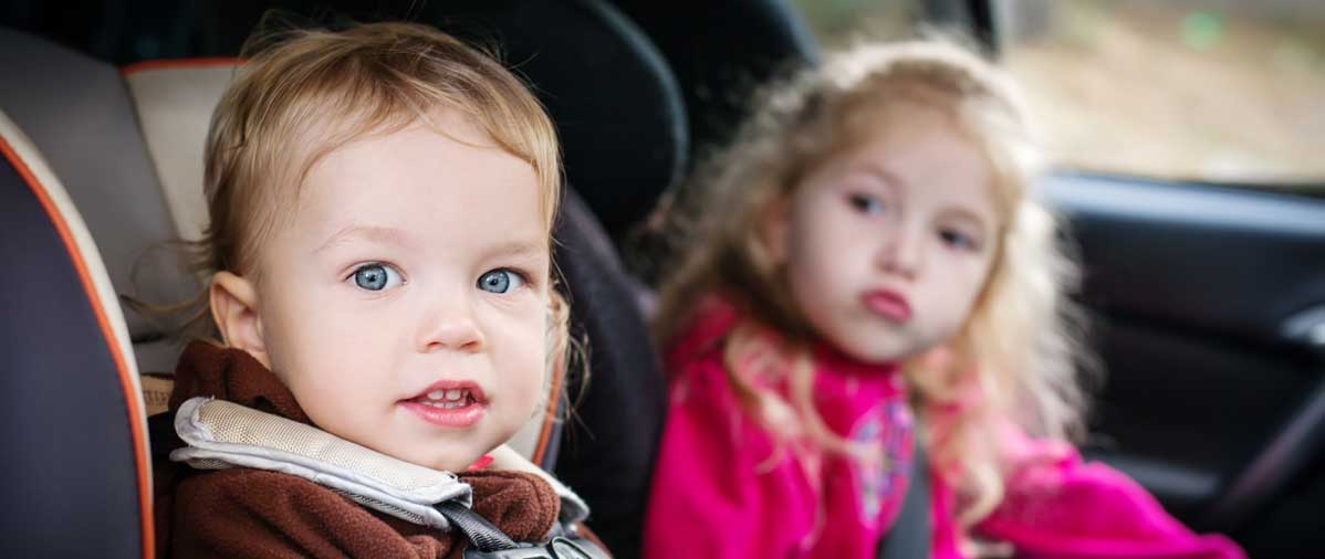 Two kids sitting in the backseat of a car in their car seats.