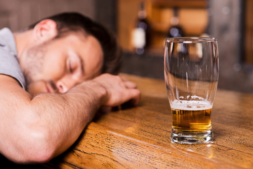 Drunk again. Drunk male customer leaning at the bar counter and sleeping while glass with beer standing near him