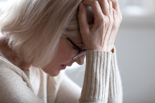 Sad tired senior woman holding head in hands feeling headache