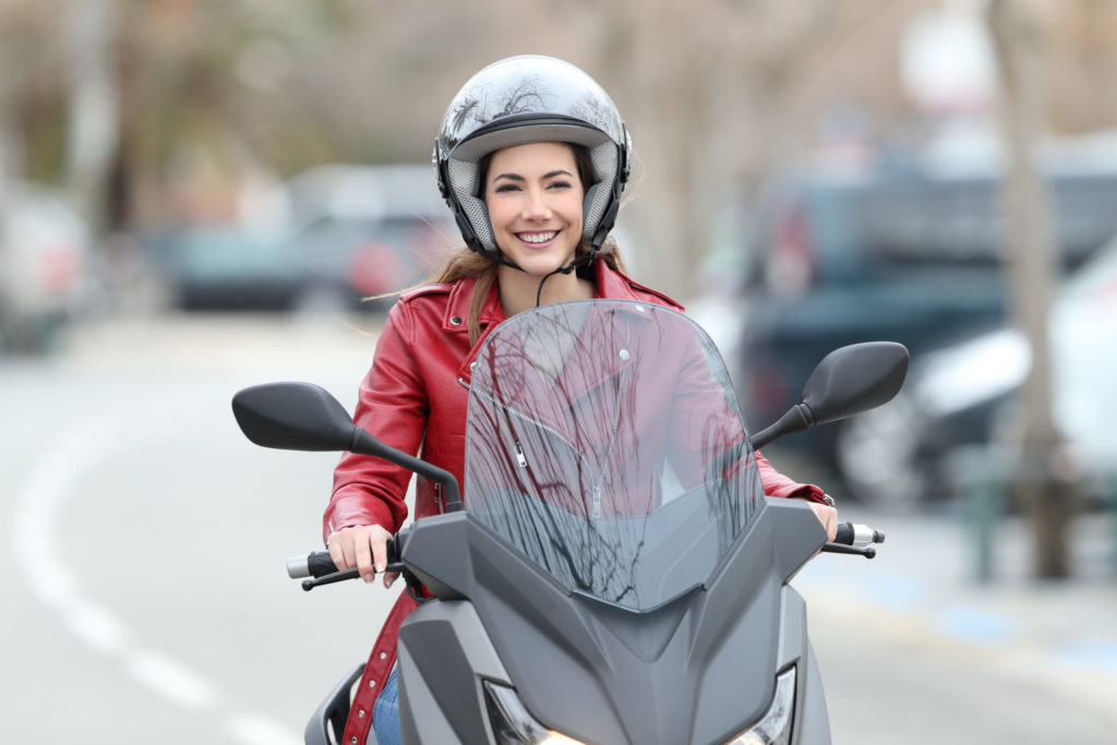 Woman wearing a helmet smiles while riding a motorcycle.
