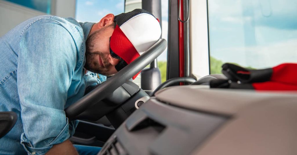 fatigued truck driver resting his head on the steering wheel of a big rig