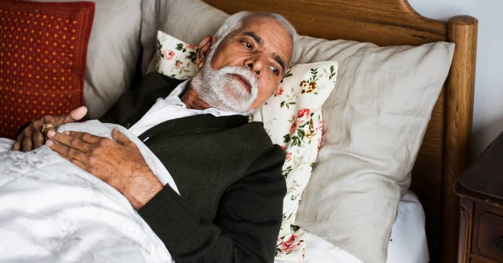 sad elderly man lying in bed at nursing home