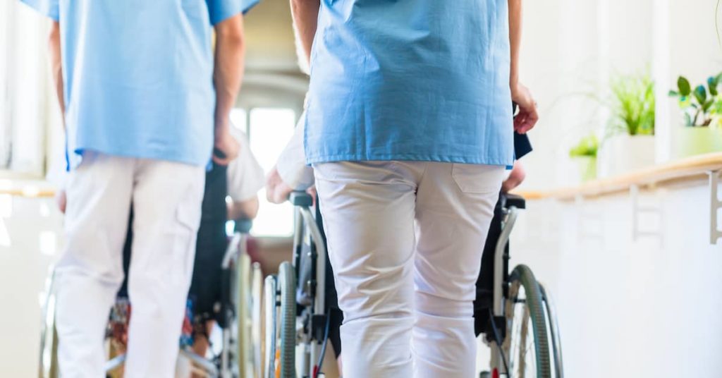 nurses pushing seniors in wheelchairs through the halls of a nursing home