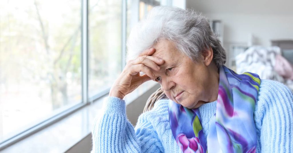 depressed elderly woman looking out the window of a nursing home