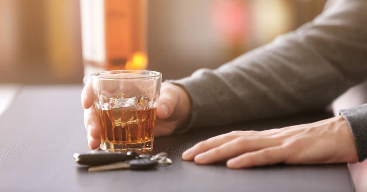 man holding liquor glass with car keys on the bar