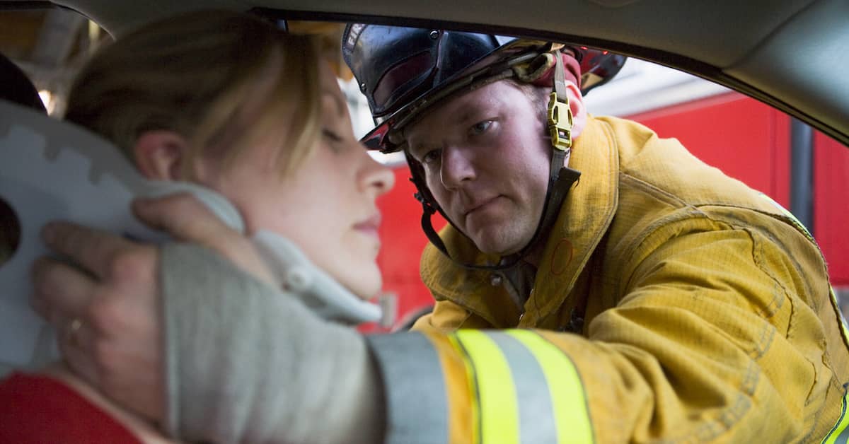 Fireman puts neck brace on woman in car accident.