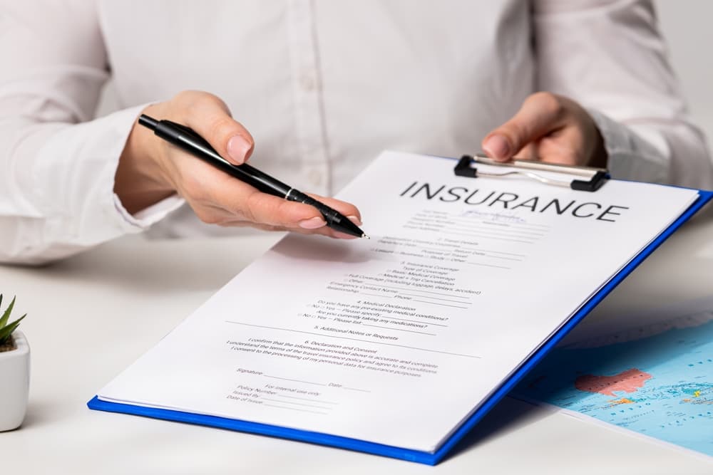 A person holding a pen and pointing to an insurance document on a clipboard, representing how insurance adjusters review claims and negotiate settlements.