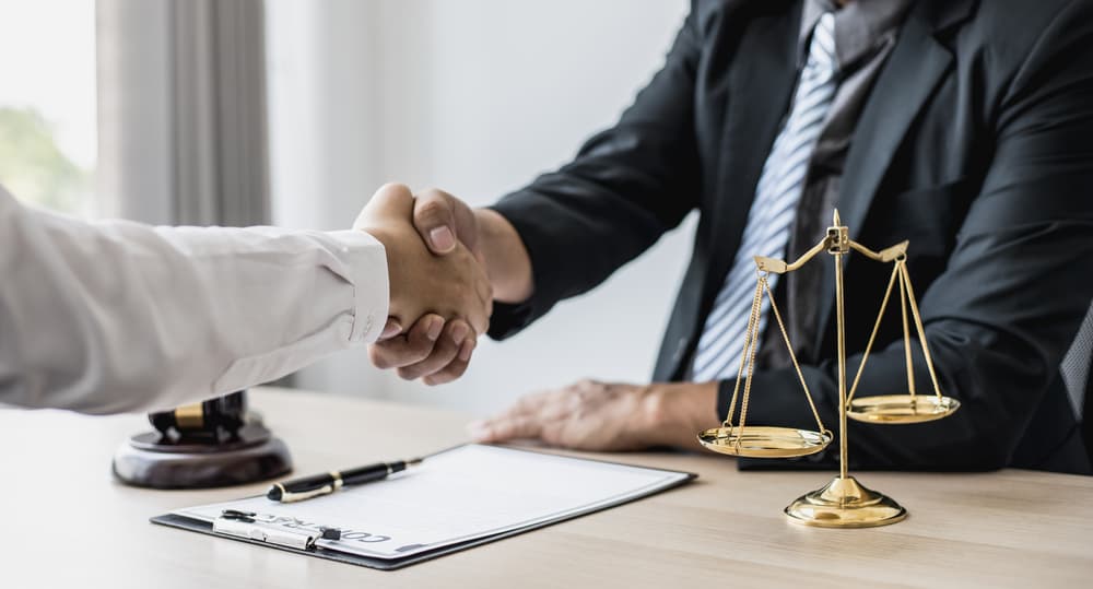 Personal injury lawyer in Bergen County shaking hands with a client after an accident consultation, legal contract, and justice scales on desk – when to hire an attorney guide.