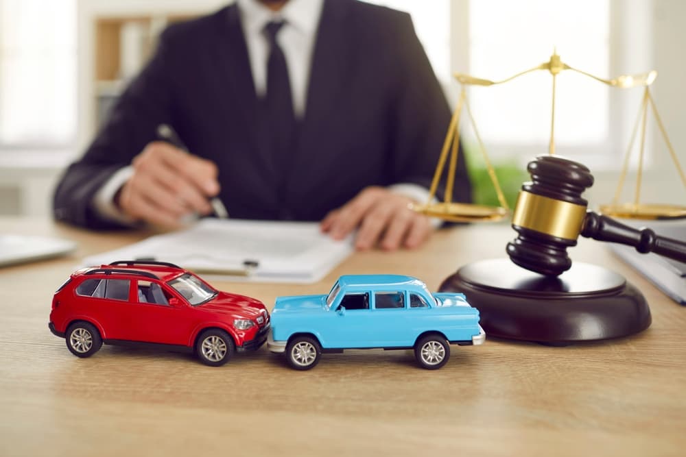 Miniature cars and a gavel on a lawyer’s desk symbolizing legal help after a car accident in Bergen County, with an attorney reviewing documents in the background.