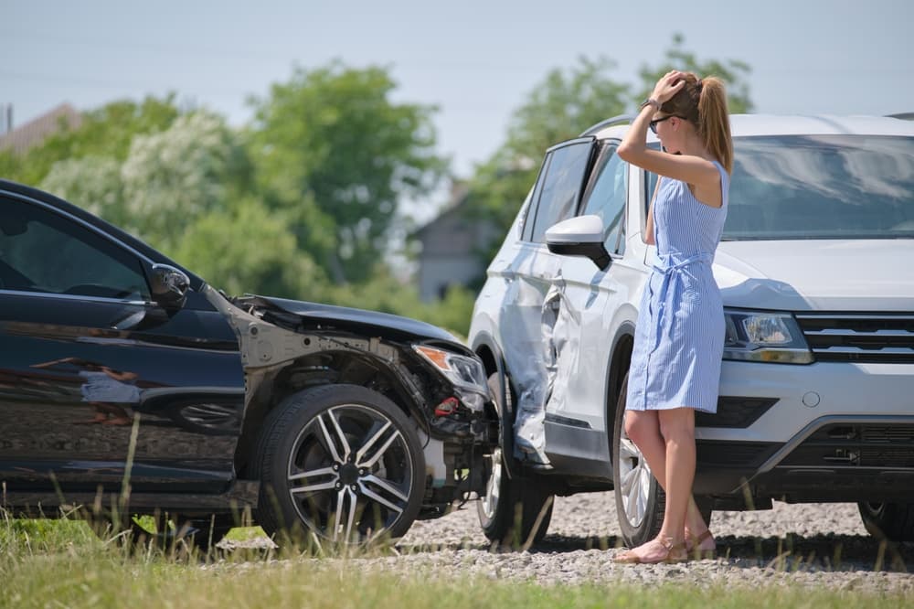 Sad female driver speaking on sellphone on street side calling for emergency service after car accident. Road safety and insurance concept