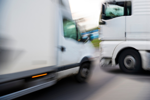 Two large trucks pass each other at high speed on a roadway, motion blur showing the potential for a collision.