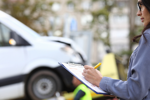 Woman writing notes on a clipboard while inspecting a white van involved in an accident, representing vehicle damage assessment.