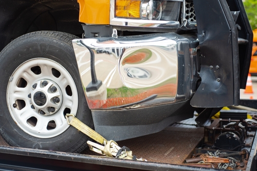 Close-up of a damaged truck bumper secured with a yellow strap on a tow truck bed after an accident.