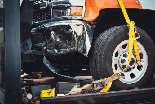 Close-up of a damaged truck wheel and bent fender secured with a yellow strap on a tow truck after an accident.