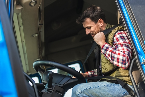 Truck driver fastening his seat belt inside a blue commercial truck cab, preparing for a trip.
