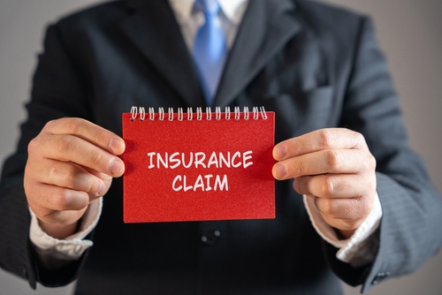 Businessman in a suit holding a red notebook with the words “Insurance Claim” printed on the cover.