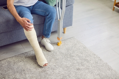 Man sitting on sofa with a full leg cast and crutches nearby, holding his injured leg.