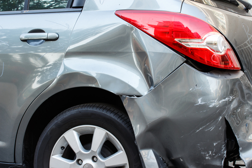 Close-up of a silver car with a large dent and scratches on the rear side panel after an accident.