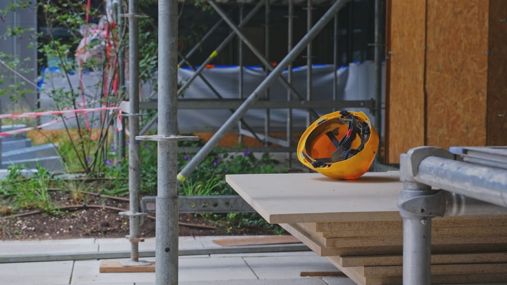 Yellow construction hard hat resting on building materials at an active construction site with scaffolding.