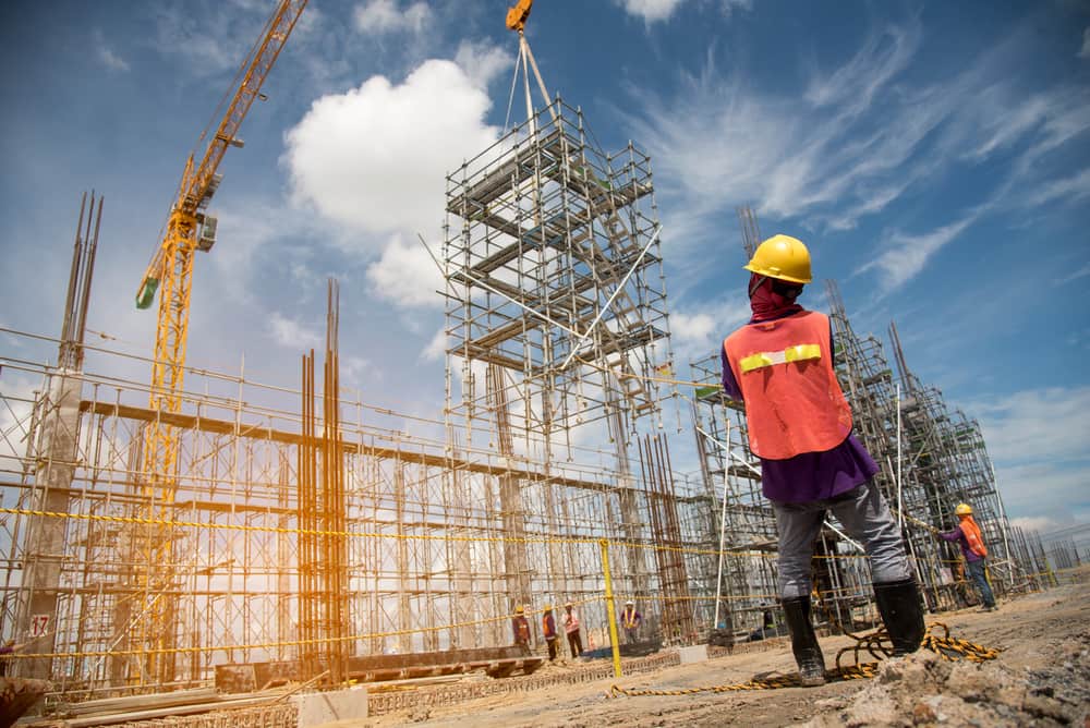 Construction workers operating around scaffolding and a tower crane at an active commercial construction site