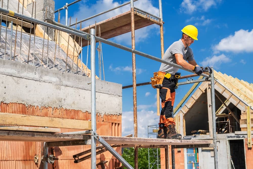 Construction worker wearing a hard hat assembling scaffolding at a residential construction site.