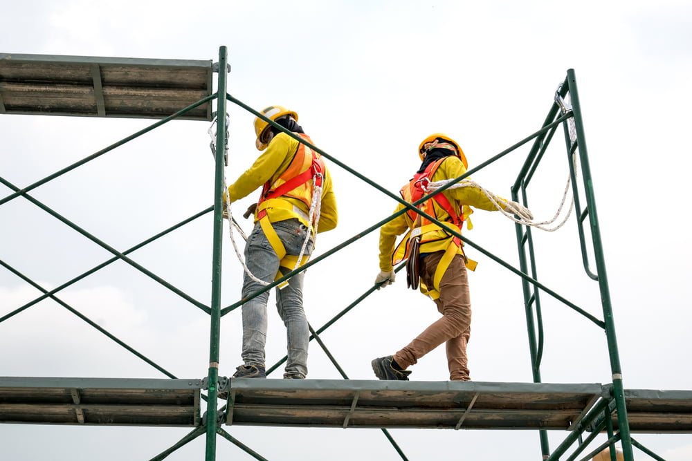 Construction workers wearing safety harnesses while working on elevated scaffolding at a job site.