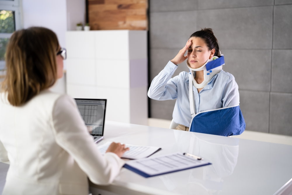 Woman wearing a neck brace and arm sling meeting with a personal injury lawyer after an accident