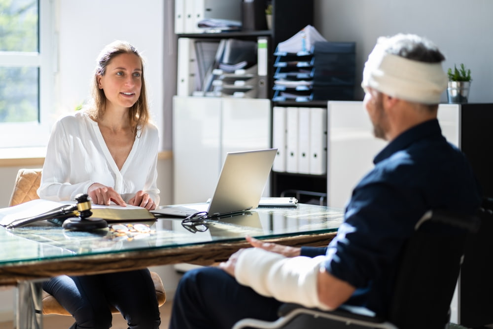Brain injury victim with head and arm injuries meeting with a personal injury lawyer to discuss a legal claim.