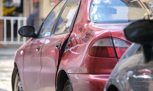 Dented car with damaged body parked on city street side. Road safety and hit and run concept