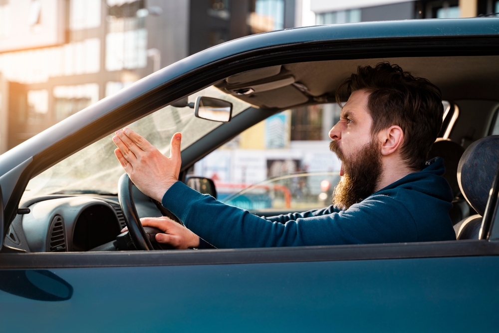 Angry driver shouting and gesturing at another motorist during a road rage incident while driving.
