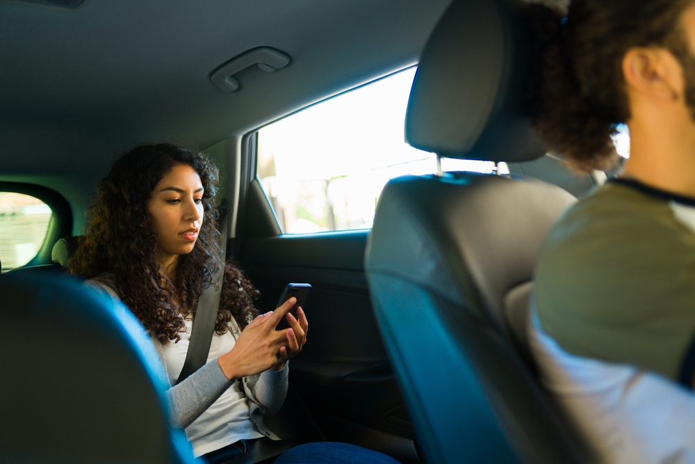 Female passenger using a smartphone while riding in the back seat of a rideshare vehicle