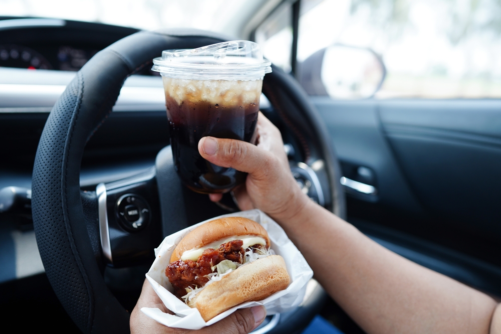 Driver holding a sandwich and a drink while operating a vehicle, illustrating distracted driving.
