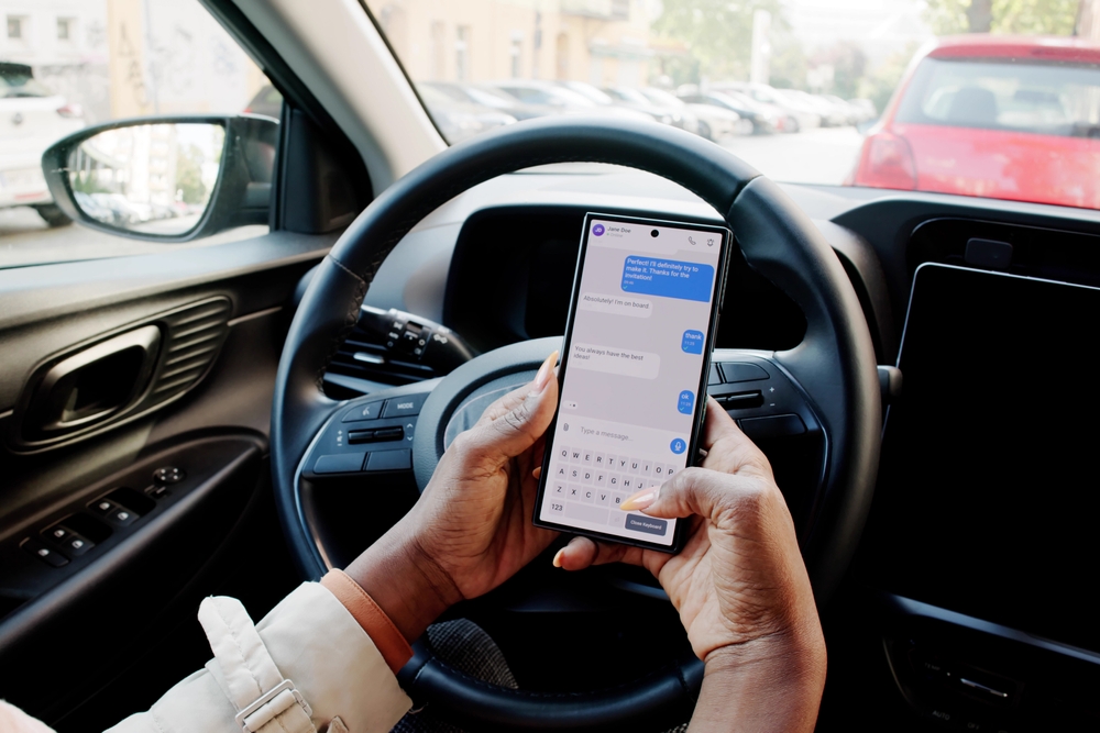 Driver holding a smartphone and sending a text message while behind the wheel of a vehicle.