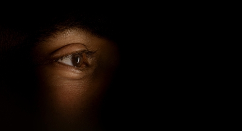 Close-up of a human eye illuminated in partial light, with a dark background, showing the eye's texture and details