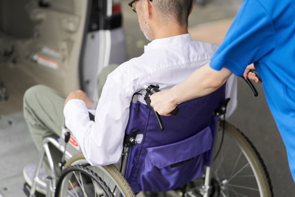 A healthcare worker pushing a man in a wheelchair near a vehicle.