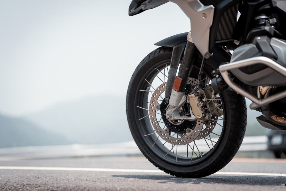 Close-up of a motorcycle front wheel and brake system on a road.